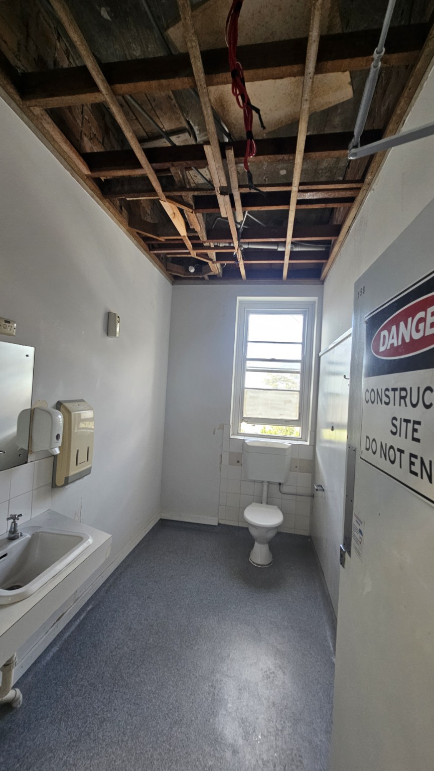 Bathroom ceiling lining removed to expose timber battens, with existing basin and toilet retained.