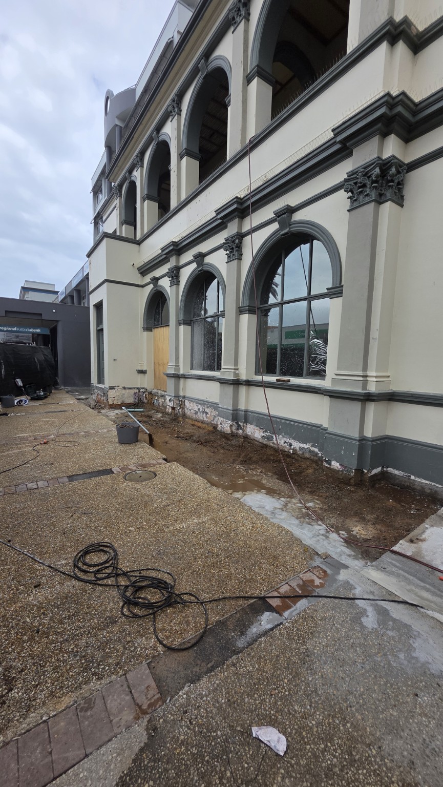 Soft demolition beside an existing two-storey building, with a narrow ground section exposed along the facade.