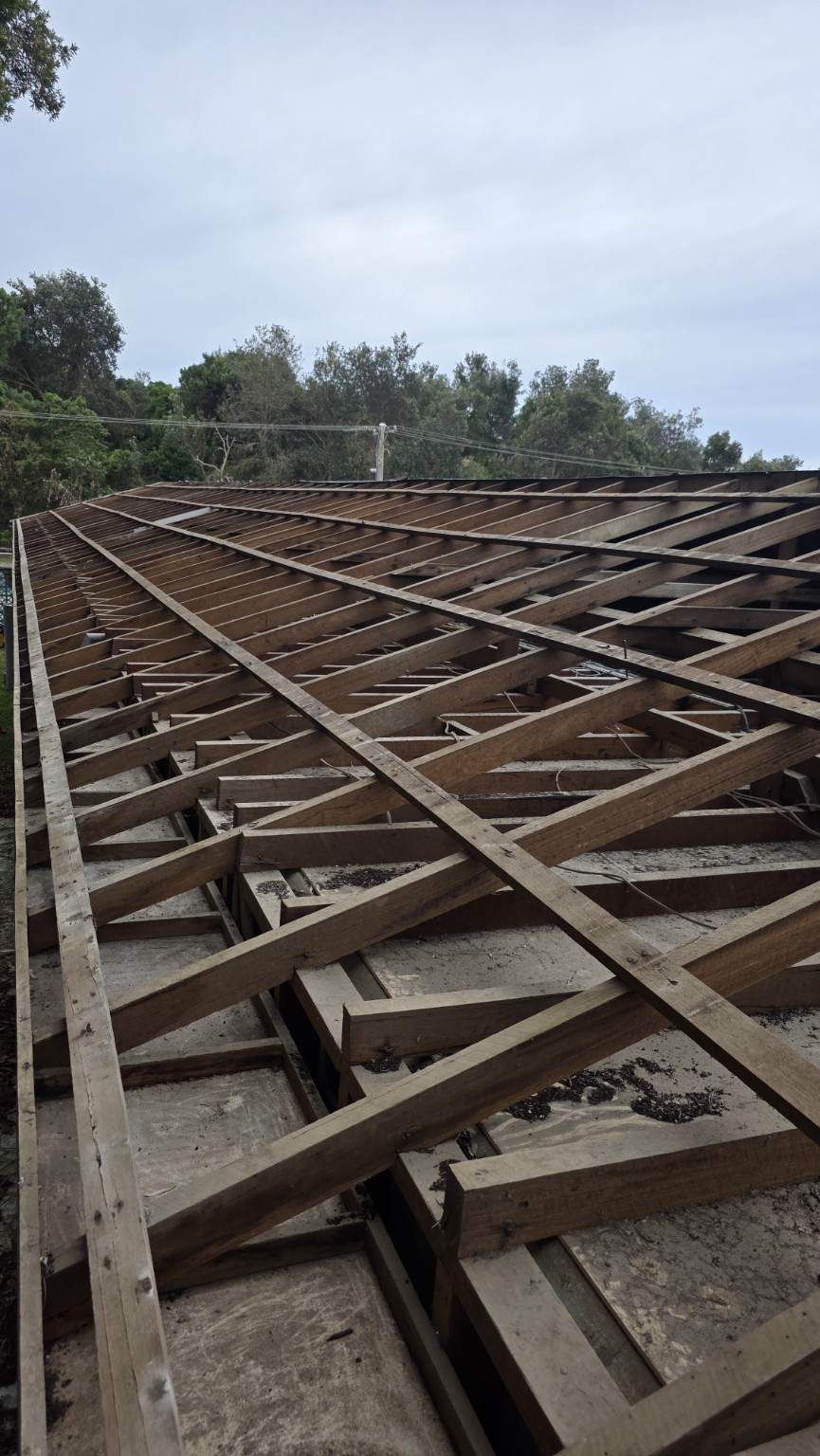 Timber roof framing exposed after roof covering removal, viewed across the length of the building.